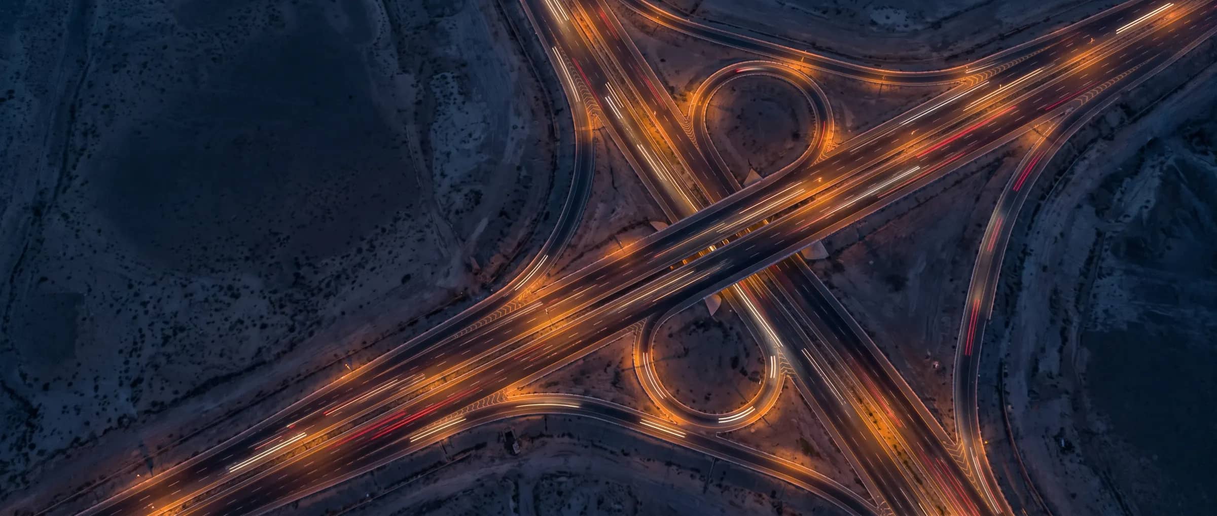 A top-down night view of a highway junction drawn by street lights and car light trails